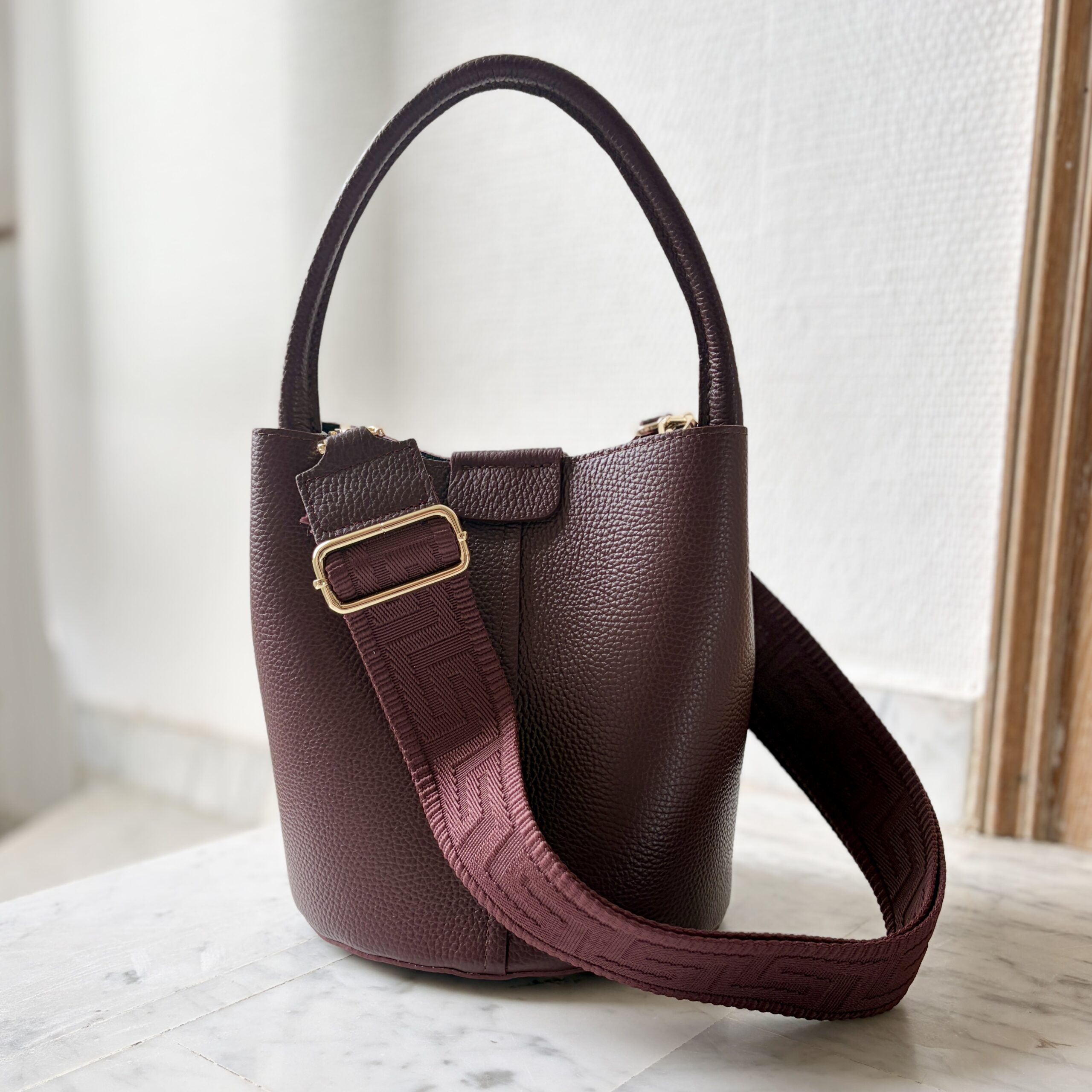 Pompeian Plum Dalu leather bucket bag with a matching patterned woven shoulder strap and gold-tone hardware.
