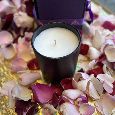 An elegant black candle surrounded by colourful rose petals on a golden surface, creating a sophisticated and romantic ambience.