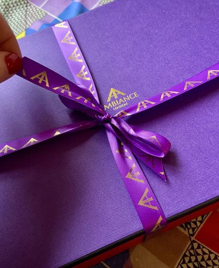 An iconic Ambiance London purple gift box, tied up with signature purple satin and gold foil ribbon, is about to be unwrapped.